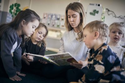 Pedagog läser i en bok för tre små elever.