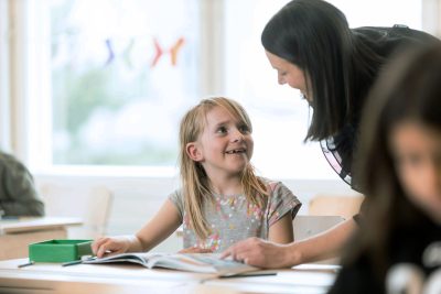 En lågstadieelev på Noblaskolan tittar glatt på sin lärare.