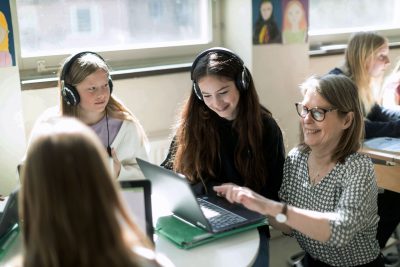 Elever på Noblaskolan sitter i ett klassrum, en av eleverna får hjälp av läraren.