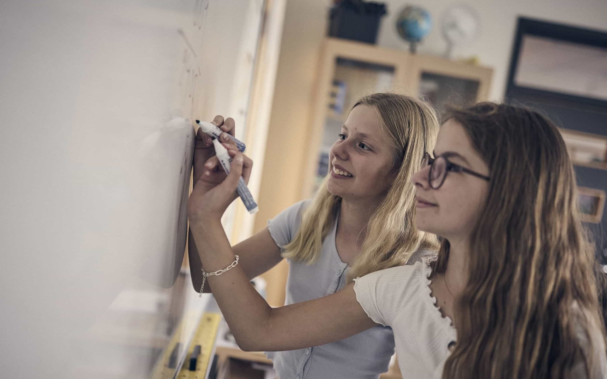 Två elever på Noblaskolan står och skriver på en whiteboard-tavla i klassrummet.