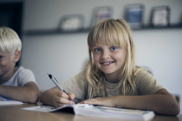 En lågstadieelev på Noblaskolan sitter i klassrummet, tittar glatt in i kameran.