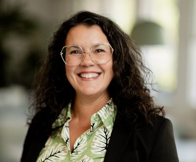 Rektor Yarmila har på sig en färglad skjorta, en svart kavaj och stora glasögon.