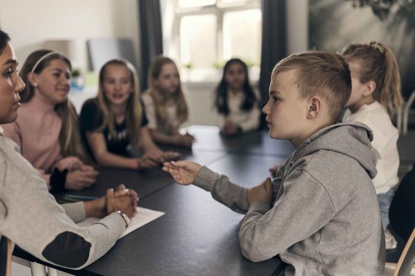 En elev sitter och pratar med sina klasskompisar och sin lärare.