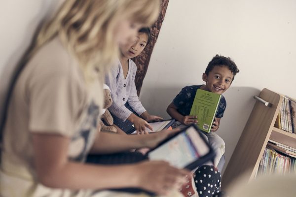 Barn i förskoleklass på Noblaskolan sitter tillsammans, två använder surfplattor och en läser en bok.