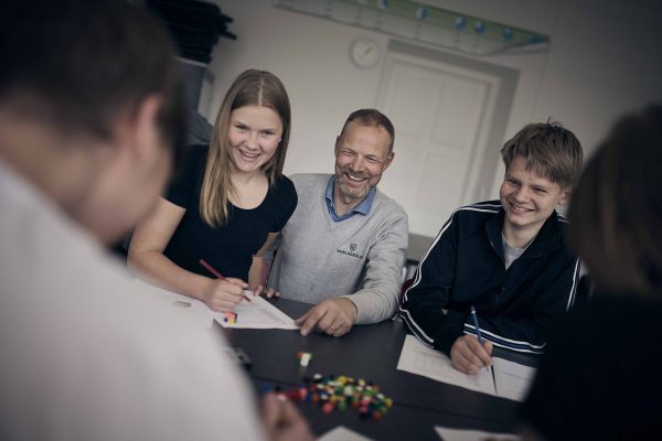 Två elever och en lärare på Noblaskolan sitter i klassrummet och skrattar.