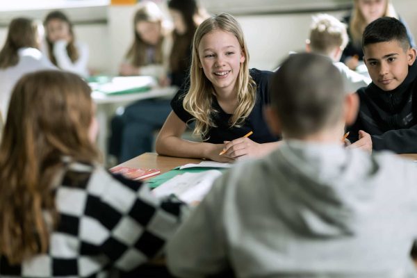 Två elever sitter i ett klassrum på Noblaskolan, i bakgrunden och förgrunden sitter fler elever.