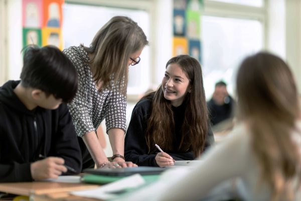 Högstadieelever sitter i ett klassrum under en lektion på Noblaskolan, en lärare hjälpen en av eleverna.