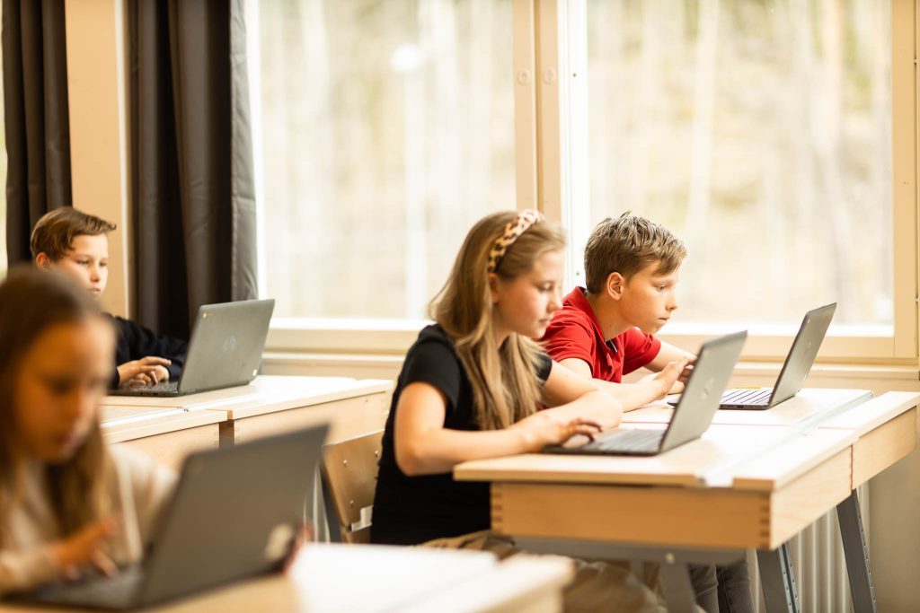 Fyra elever sitter i sitt klassrum med sina skoldatorer och studerar