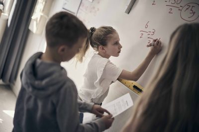 Elever står framme vid tavlan i ett klassrum och löser ett matteproblem.
