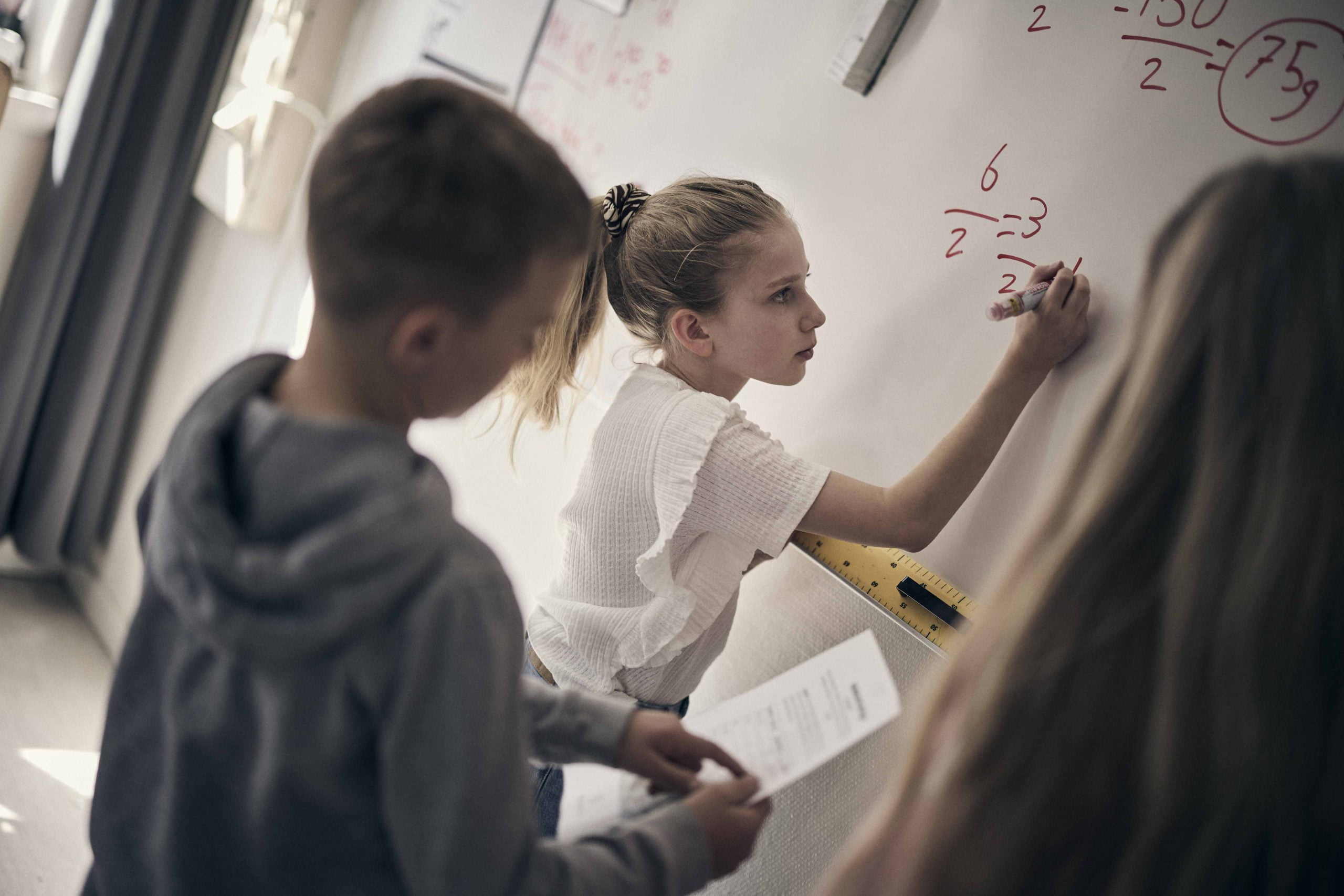 Elever står framme vid tavlan i ett klassrum och löser ett matteproblem