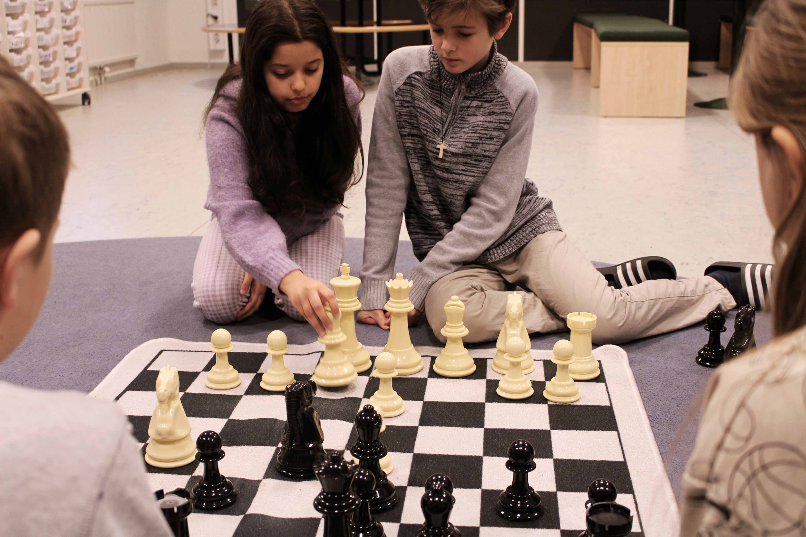 Fyra elever på Noblaskolan spelar schack på en stor schackmatta på golvet.