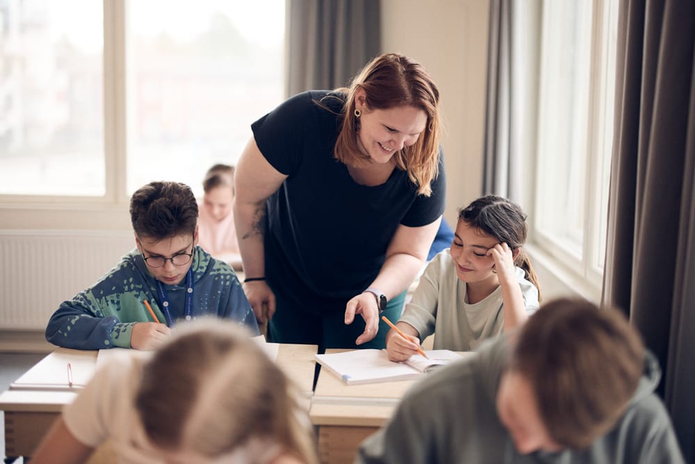 Lärare hjälper elev som sitter vid sin bänk i klassrummet.
