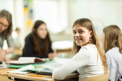 En elev sitter vid sin skolbänk vid sina klasskompisar och ler.