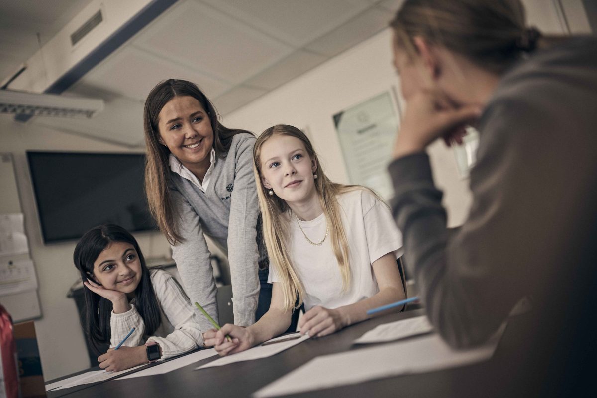 Lärare på Noblaskolan står vid ett bord och pratar med elever.
