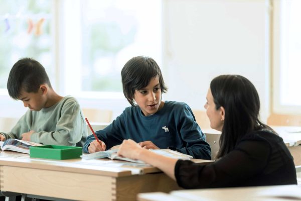 Två elever på Noblaskolan i ett klassrum, den ena får hjälp av läraren.