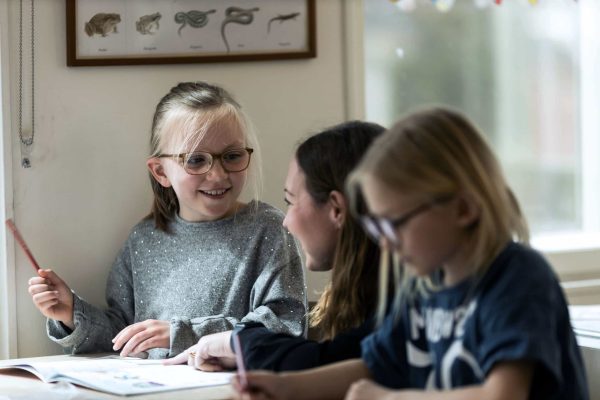 Två elever på Noblaskolan som sitter och studerar i ett klassrum, den ena får hjälp av läraren.