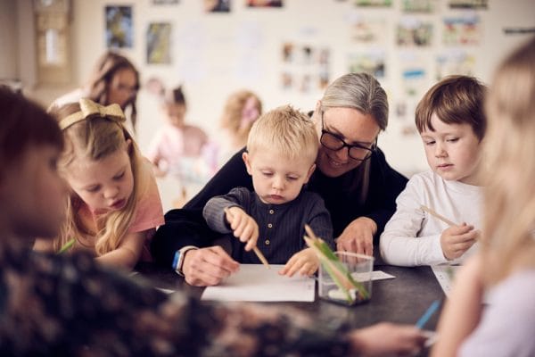 Pojke sitter i knä på pedagog när de målar på förskolan.