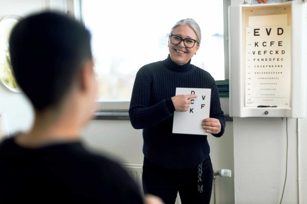 Skolsköterskan på Noblaskolan står vid en syntavla och undersöker en elevs syn.