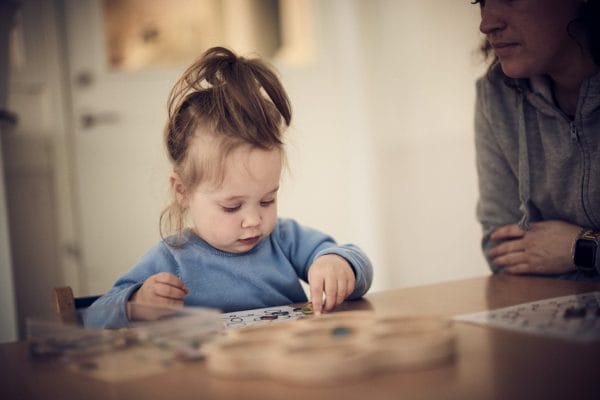 Barn i blå tröja och tofs som leker vid ett bord på förskolan